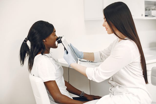 Healthcare professional examining a patient’s face with a medical device.